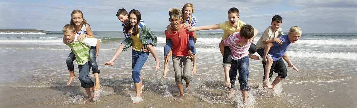 Gruppe von bunt gekleideten Jugendlichen läuft am Strand durch Ausläufer der Wellen.