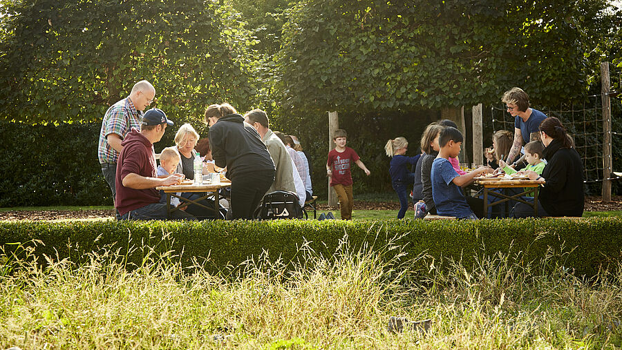 Erwachsene essen mit Kindern und Jugendlichen draußen im Garten