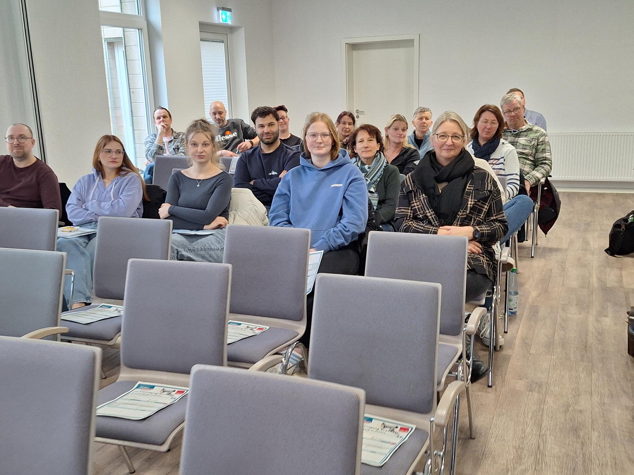 Mehrere Mitarbeitende der Jugendhilfe Collstede sitzen in einem Veranstaltungsraum auf Stuhlreihen und verfolgen aufmerksam eine Präsentation während der Mitarbeitendenversammlung.